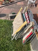 Folded view of three aluminum frame folding chairs and one lounger with striped fabric, stacked on grass and patio.