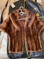 Brown fur stole hanging on white plastic hanger with silky brown lining visible inside, placed on a black garment bag.