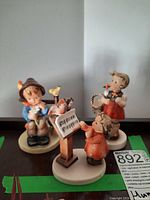 Three Hummel figurines shown together on a table, highlighting their size and colors.