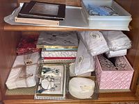 Shelf with stacked vintage napkins and hand towels, coasters, boxed items, and a pink plastic Kleenex holder