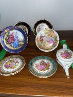 Photo showing six small Limoges plates with varied colored rims and romantic/classical scenes, plus a porcelain Limoges bellows figurine