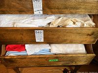 Two drawers of wooden furniture partially open filled with folded white and cream linens, some with lace edges and embroidery.