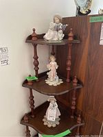 Three figurines displayed on a dark wood corner shelf, showing relative sizes and positioning