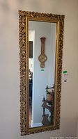 Front view of rectangular wall mirror with ornate gold frame and clear reflective glass showing a part of the room in reflection.