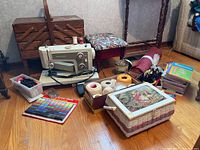 Overview of Kenmore sewing machine on the floor with sewing supplies, sewing box, foot stool, and puzzle books