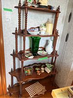 Side view showing entire wood shelving unit with five shelves, each with scalloped edges, supported by vertical spiral turned columns, with decorative finials on top corners.