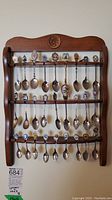 Front view of the wooden rack displaying all 24 souvenir spoons hung neatly in 3 rows.