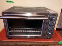 Full frontal view of stainless steel toaster oven showing glass door, handle, and part of control panel with knobs