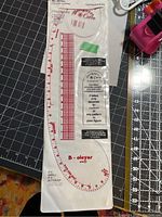 Top view of Designer’s Curve altering ruler in original plastic sleeve with red markings and measurement scales