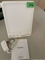 Lastar light therapy lamp with power adapter and user manual placed on table.
