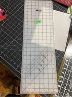 Top view of the clear plastic cutting ruler showing grid lines, angle markings, and size measurements.