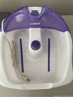 Photo of Conair electric foot bath in white and purple, showing top view with power cord wound beside it.