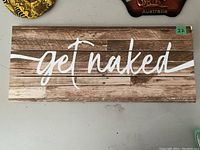 Full front view of rectangular wooden wall sign with 'get naked' text in white against a wood plank background.