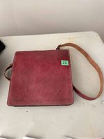 Brown leather purse with flap closed and visible shoulder strap