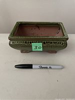 Front and side view showing green speckled glaze and raised feet with marker for size reference