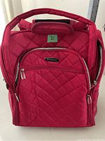 Front view of the red quilted soft suitcase showing the padded handle and front zippered pocket.
