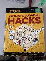 Front cover of the 'Ultimate Survival Hacks' book by Outdoor Life, showing survival tool illustrations and title.