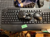 Black wireless keyboard with black wireless mouse and USB receiver placed on keyboard. Mouse battery compartment open.