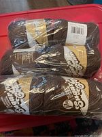 Four skeins of brown wrapped yarn in plastic packaging brand Loops & Threads Sugar 'n Cream.
