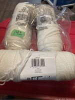 Two skeins of white yarn in plastic packaging with labels, medium weight yarn visible