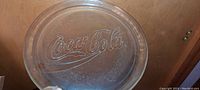Clear heavy glass serving plate embossed with Coca-Cola logo, showing the embossed lettering and texture.
