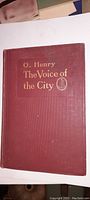 Front cover of the maroon hardcover book titled 'The Voice of the City' by O. Henry with gold embossing.