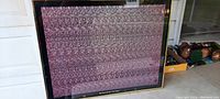 Framed poster with complex stereogram pattern visible, wall-mounted outdoors in partial shade.