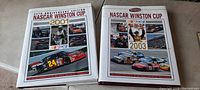 Two hardcover NASCAR Winston Cup books from 2001 and 2003 with dust jackets, placed side by side on a grey carpeted floor.