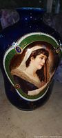 Front view showing painted female portrait oval medallion and decorative gold leaf elements on blue base.