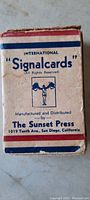 Photo of the front of the cardboard box containing the deck labeled 'International Signalcards' by The Sunset Press, San Diego, California.