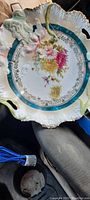 Full view of early 1900s serving plate showing scalloped edges, turquoise band, floral center, and embossing.