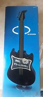 Blue box featuring an image of the black rotating guitar and rotation arrows, showing the closed packaging of the musical display item.