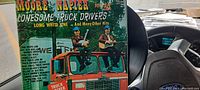 Photo of the LP sleeve showing two men sitting on top of a truck cab with title 'Moore & Napier Lonesome Truck Drivers'. Vintage trucker style graphic with orange, green, and white lettering.