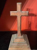 Front view of the wooden cross on a tiered base showing shape, texture, and state of dust.