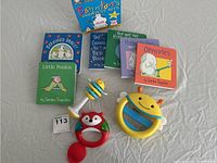 Five Sandra Boynton board books and three baby rattles displayed on a sheet.