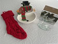 Overview of all three items in the lot: ceramic snowman serving dish, knitted red stocking, and Pier 1 glass reindeer decoration.