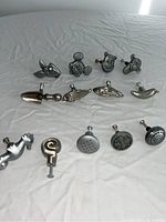 Overview image showing all 13 metal cupboard knobs in a group on a table with neutral background. Includes Disney character and themed knobs.