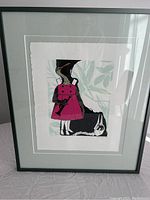 Framed print showing a figure in a pink dress next to a black animal with leafy background.