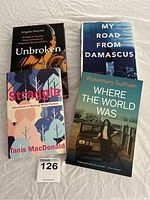 Front covers of four memoir books laid out on a white cloth surface: 'Unbroken', 'My Road from Damascus', 'Where The World Was', and 'Straggle'.