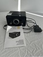 Scansonic R2 radio with instruction manual and power adapter placed on a white surface, showing front and top of radio, manual beside it, power adapter plugged in.