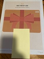 Gift card showing orange background with red bow graphic, $100 value displayed, partially obscured redemption code.