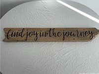 Full view of the wooden sign showing "find joy in the journey" phrase in black cursive lettering on a rustic plank.