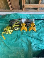 Full view of the hydraulic trolley jack, two yellow jack stands, and two yellow ratchet straps laid on a green tarp.