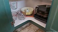 Yellow Bundt pan, muffin tins, loaf pans, measuring cups visible inside a green cabinet corner.