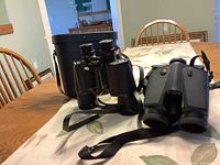 Photo showing two pairs of binoculars on a table along with their cases.
