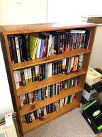 Front view of the bookshelf filled with books showing the four solid wood shelves.