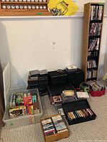 Wide view showing wooden CD shelf, stacked DVDs, plastic containers with VHS tapes and CDs on carpeted floor