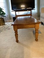 Side view showing turned wooden leg of coffee table, supporting rectangular top with visible wood grain.