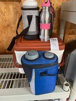 Portable cooler box, insulated blue soft cooler bag with bottle holders, and two stainless steel travel bottles.