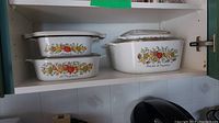 Set of four Corningware dishes with lids displayed on a shelf.